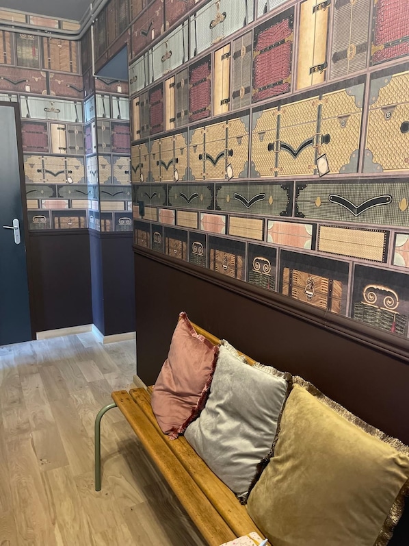 Une pièce avec un banc en bois, un mur recouvert de boîtes de rangement décorées, et une porte donnant sur un autre espace.