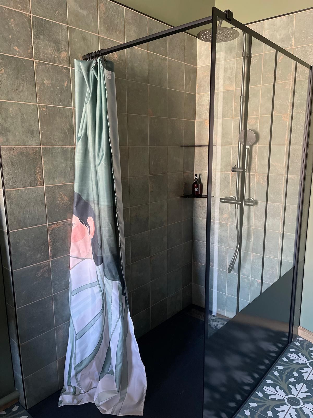 Un espace douche fermé par des parois en verre, équipé d’un rideau de douche orné d’un motif floral.