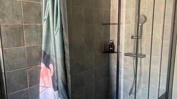 Un espace douche fermé par des parois en verre, équipé d’un rideau de douche orné d’un motif floral.