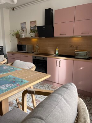 Une cuisine moderne avec des meubles roses, un four à micro-ondes, un évier et un coin repas comprenant une table et des chaises.