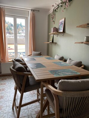 Un coin repas avec une table et des chaises en bois, une vue par la fenêtre et un mur avec des étagères.