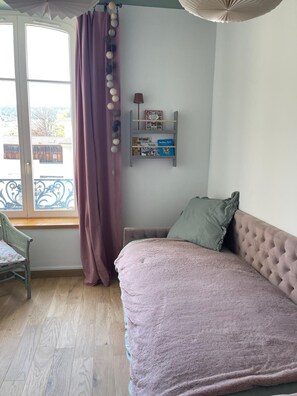 Une chambre à coucher avec un lit, une fenêtre avec des rideaux, une chaise et une étagère remplie de livres.