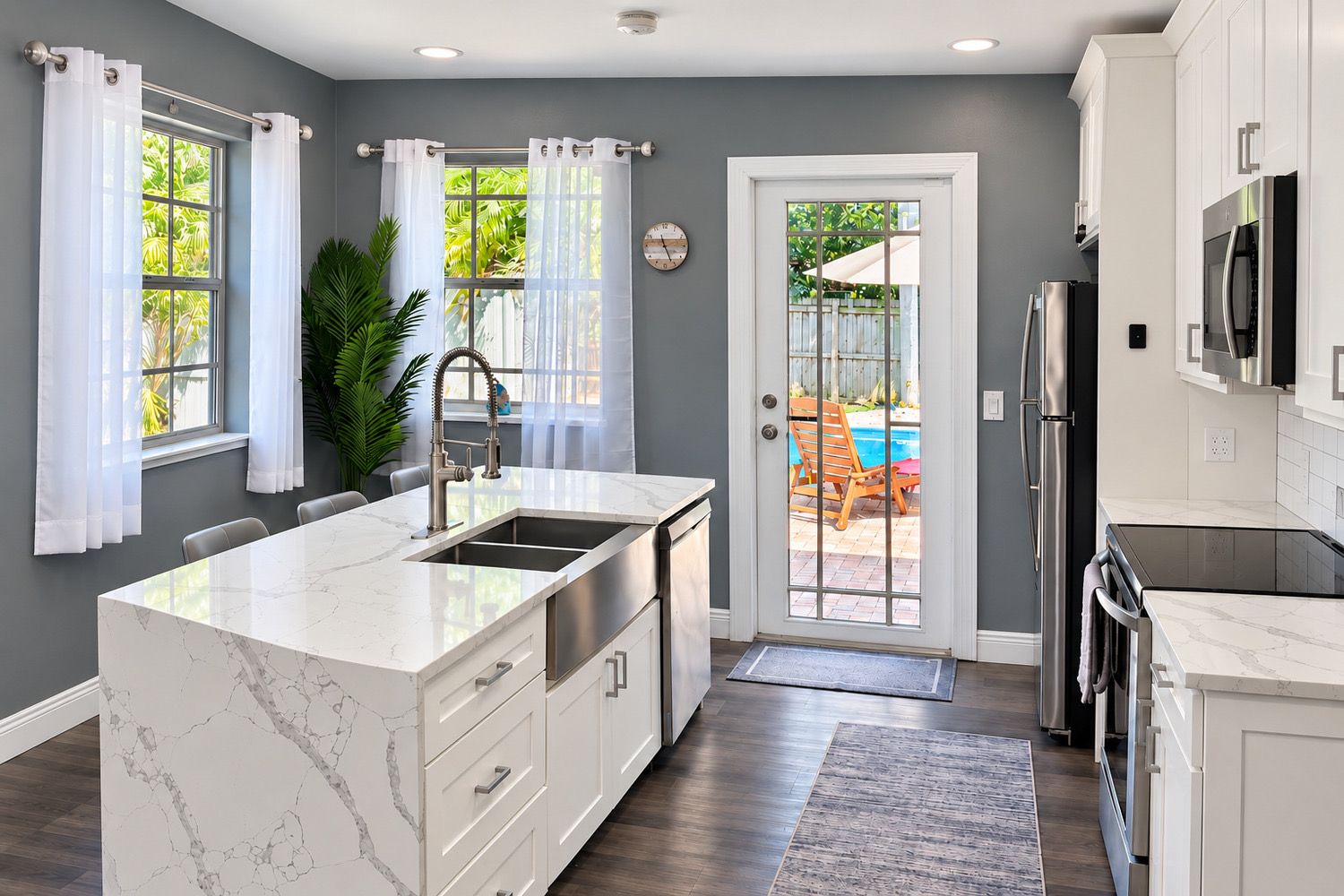 A modern kitchen with a marble countertop, stainless steel appliances, and a view of a backyard with a pool.