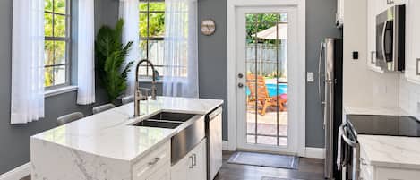 A modern kitchen with a marble countertop, stainless steel appliances, and a view of a backyard with a pool.