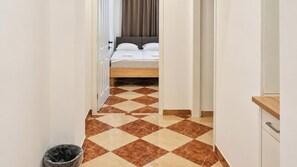 A hotel corridor with a checkered floor leading to a bed with a wooden headboard. - Vienna at Your Pace 1BR and Living Room (Vienna)