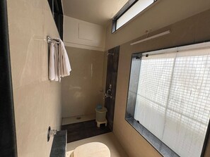 A compact bathroom with a shower, a toilet, and a window with a grid pattern. - Classic Hotel Saubhagyashanti (Nashik)