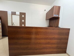 A reception desk with a wooden finish, a white wall, and a door with a check-in/out sign. - Classic Hotel Saubhagyashanti (Nashik)