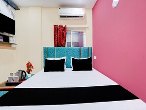 A hotel room with a bed, a window with curtains, an air conditioning unit, and a small table with a kettle and cups. - Deluxe Room Hotel Khushi in (Bhubaneshwar)