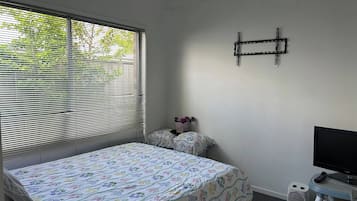 A bedroom with a bed, a TV, and a window with blinds.