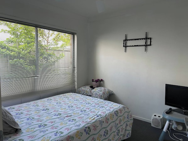 Un dormitorio con cama, televisor y ventana con persianas.