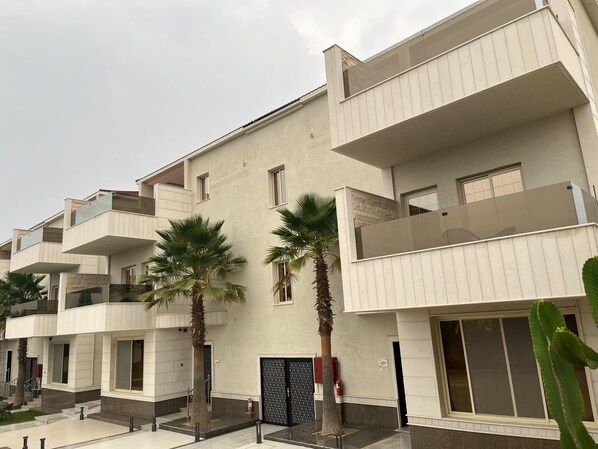 A multi-story residential building with balconies, palm trees, and a fire extinguisher.