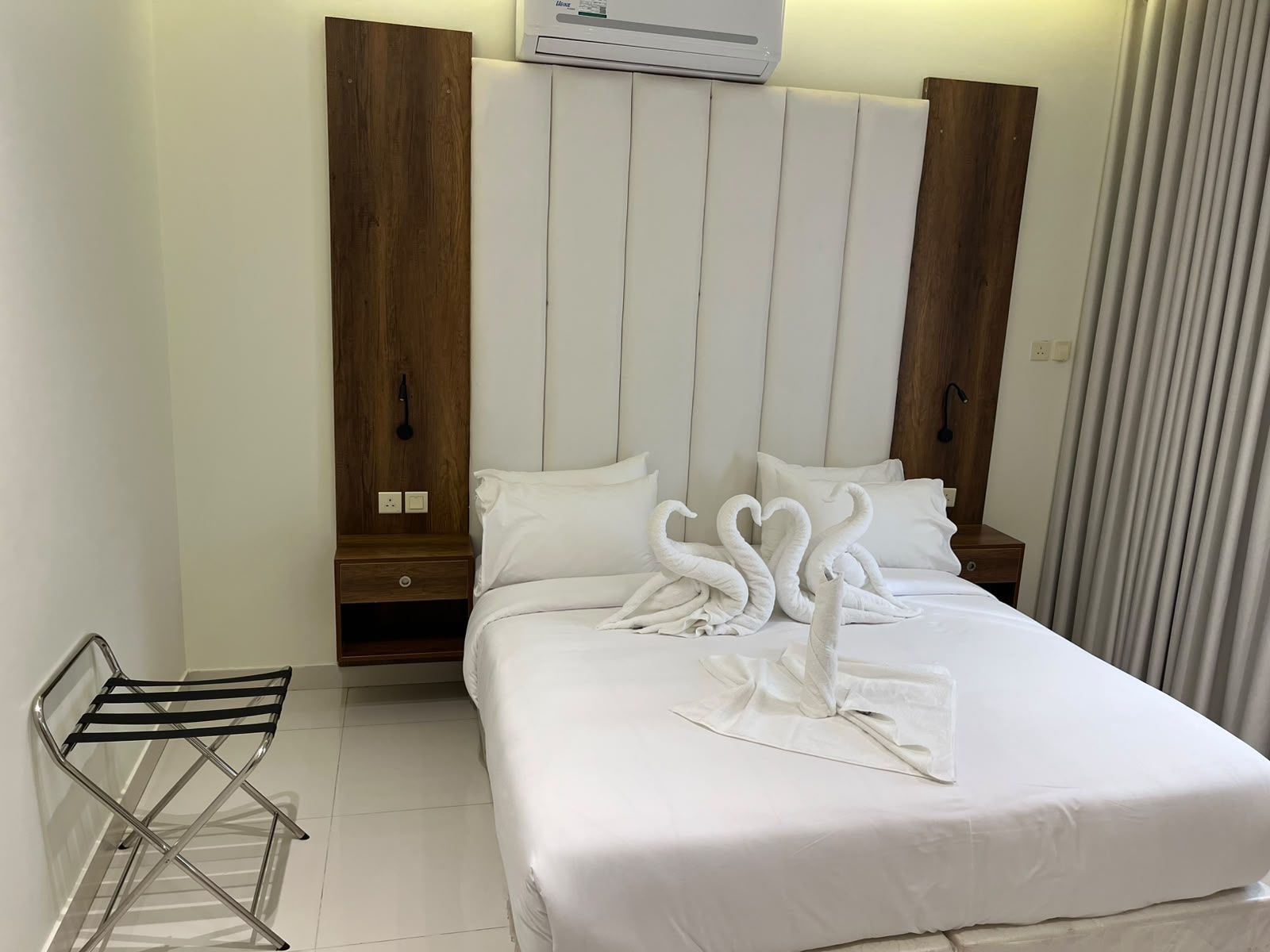 A hotel room with a bed, a wooden wardrobe, a nightstand, and a towel sculpture.