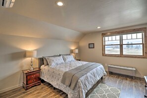 A bedroom with a bed, nightstands, a bench, a window with a view, and a ceiling light. - Creekside Apartment in Kalispell on 5 Acres (Kalispell)