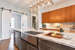 A modern kitchen with a large island, stainless steel appliances, wooden cabinets, and a hanging light fixture. - Nashville-themed House 12 South Gulch Sleeps 12 (Nashville)