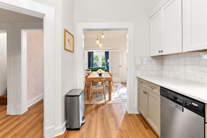 A modern kitchen with white cabinetry, a dishwasher, and a dining area with a wooden table and chairs. - East Nashville Craftsman - Sleeps 10 - Media Room (Nashville)