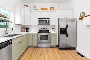 A modern kitchen with white cabinets, stainless steel appliances, and a wooden floor. - East Nashville Craftsman - Sleeps 10 - Media Room (Nashville)