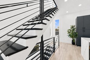 En modern trappa med svarta räcken och vita väggar, som leder upp till ett rum med ett mörkt skåp och en krukväxt.