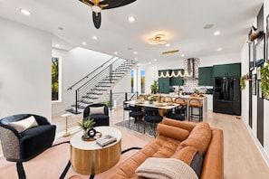 A modern living room with a sofa, coffee table, and a dining area with chairs and a table. - Rooftop Game Room Near Broadway Sleeps 10 (Nashville)