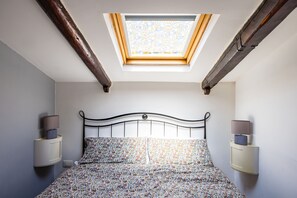 A bedroom with a skylight, a bed with floral bedding, and bedside lamps. - Alessio's House by Napoliapartments (Naples)