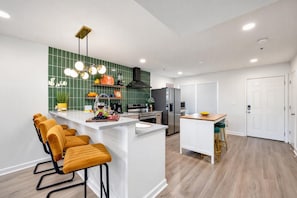 A modern kitchen with a central island, bar stools, a refrigerator, and a stove. - Walkable Sobro House - Gated Parking - Sleeps 8 (Nashville)