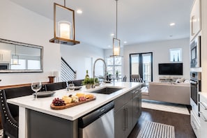 A modern kitchen with a central island, built-in appliances, and a dining area with a bench. - Gulch Rooftop Fire pit Putting Green - Sleeps 12 (Nashville)