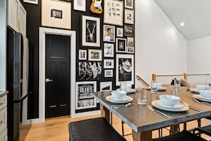 A dining area with a long table set for four, framed artwork on the wall, and a black door. - Rooftop Patio Home Near Broadway Vandy - Sleeps 12 (Nashville)
