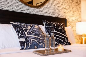 A hotel room with a bed, two pillows, a bedside table with two bottles and a candle, and a wall with a textured pattern. - Skyline Views House - 4 Ensuites - Sleeps 12 (Nashville)
