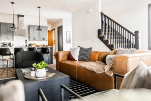Un salon moderne avec un canapé en cuir, une table basse agrémentée d’une plante et un escalier doté d’une rampe noire.