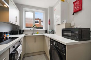 Una cocina compacta con lavavajillas integrado, microondas y ventana con vista a un edificio de ladrillo.