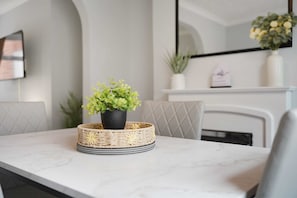 A dining table with a woven basket containing a green plant, set against a white wall with a framed picture and a mirror. - Albert Street 2BR Free Wifi by Stay With Us (Chester-le-Street)