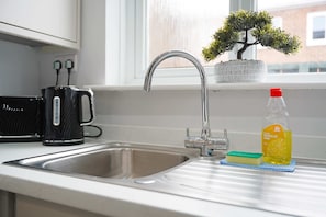 A kitchen sink with a modern faucet, a kettle, a bottle of washing up liquid, and a small potted plant. - Albert Street 2BR Free Wifi by Stay With Us (Chester-le-Street)