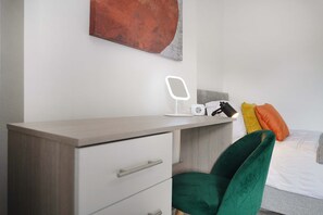 A modern bedroom with a wooden desk, a green chair, a bedside table with a lamp, and a bed with colorful pillows. - Cozy 2BR Home Sleeps 5 With Wifi by Stay With Us (Wigan)