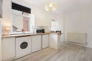 A modern kitchen with a washing machine, microwave, and a dining area with a table and chairs. - Cozy 2BR Home Sleeps 5 With Wifi by Stay With Us (Wigan)