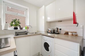 A modern kitchen with a built-in washing machine, a toaster, and a kettle. - Cozy 2BR Home Sleeps 5 With Wifi by Stay With Us (Wigan)