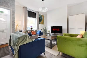 Un soggiorno moderno con televisione, divano, poltrona, un'area pranzo con tavolo e una grande finestra con tende.