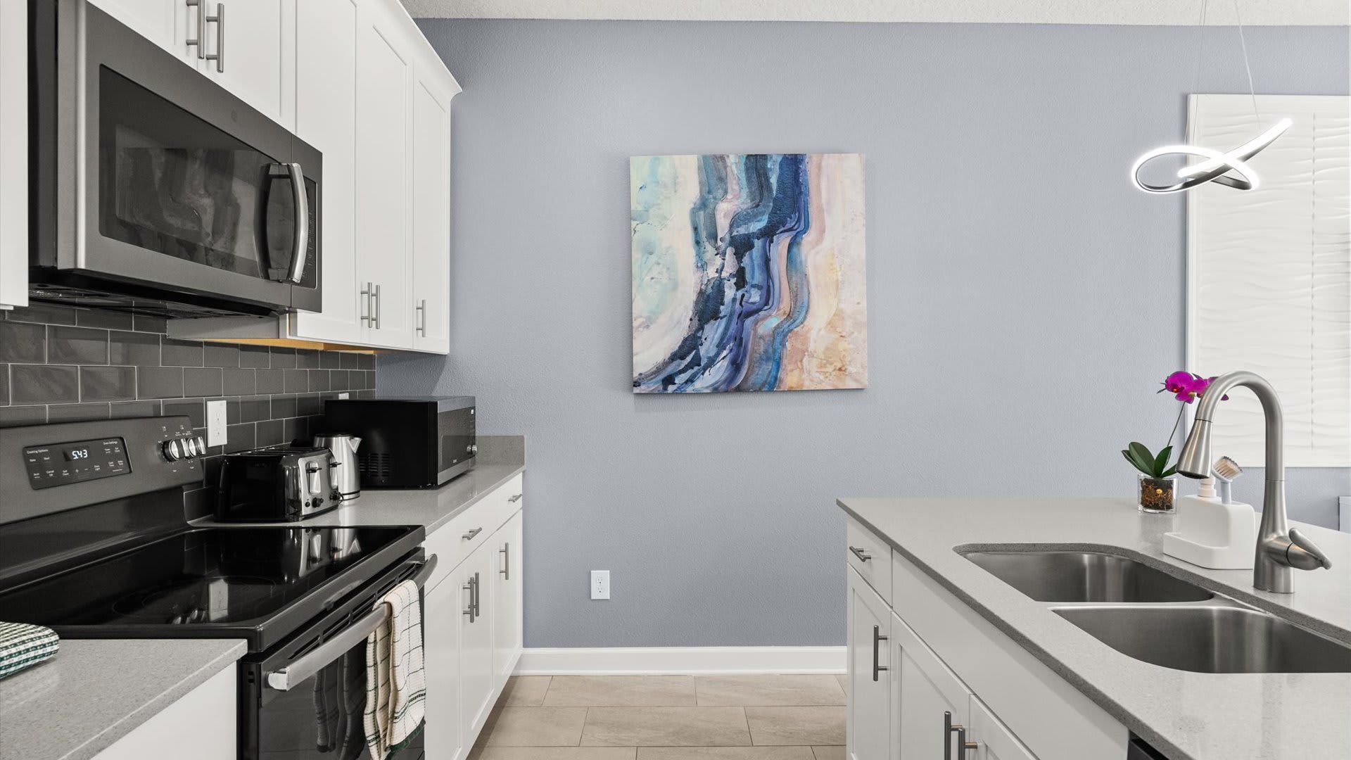 Een moderne keuken met een grijze wand, roestvrijstalen apparatuur en een abstract schilderij.