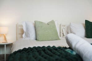 A bed with white bedding and a green pillow, a bedside table with a lamp, and a dark green blanket. - Cosy Blackhall 2BR Sleeps 5 By Stay With Us (Hartlepool)