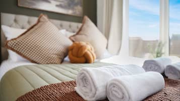 Una cama bien hecha con toallas blancas enrolladas, una manta marrón texturizada y almohadas decorativas.