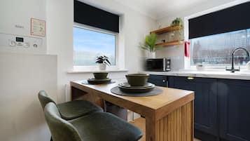 A modern kitchen with a wooden table, two chairs, a microwave, and a window with a view.
