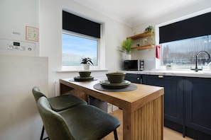 A modern kitchen with a wooden table, two chairs, a microwave, and a window with a view. - Spacious 4BR Near Hornsea Museum Sleeps 8 Wifi (Hornsea)