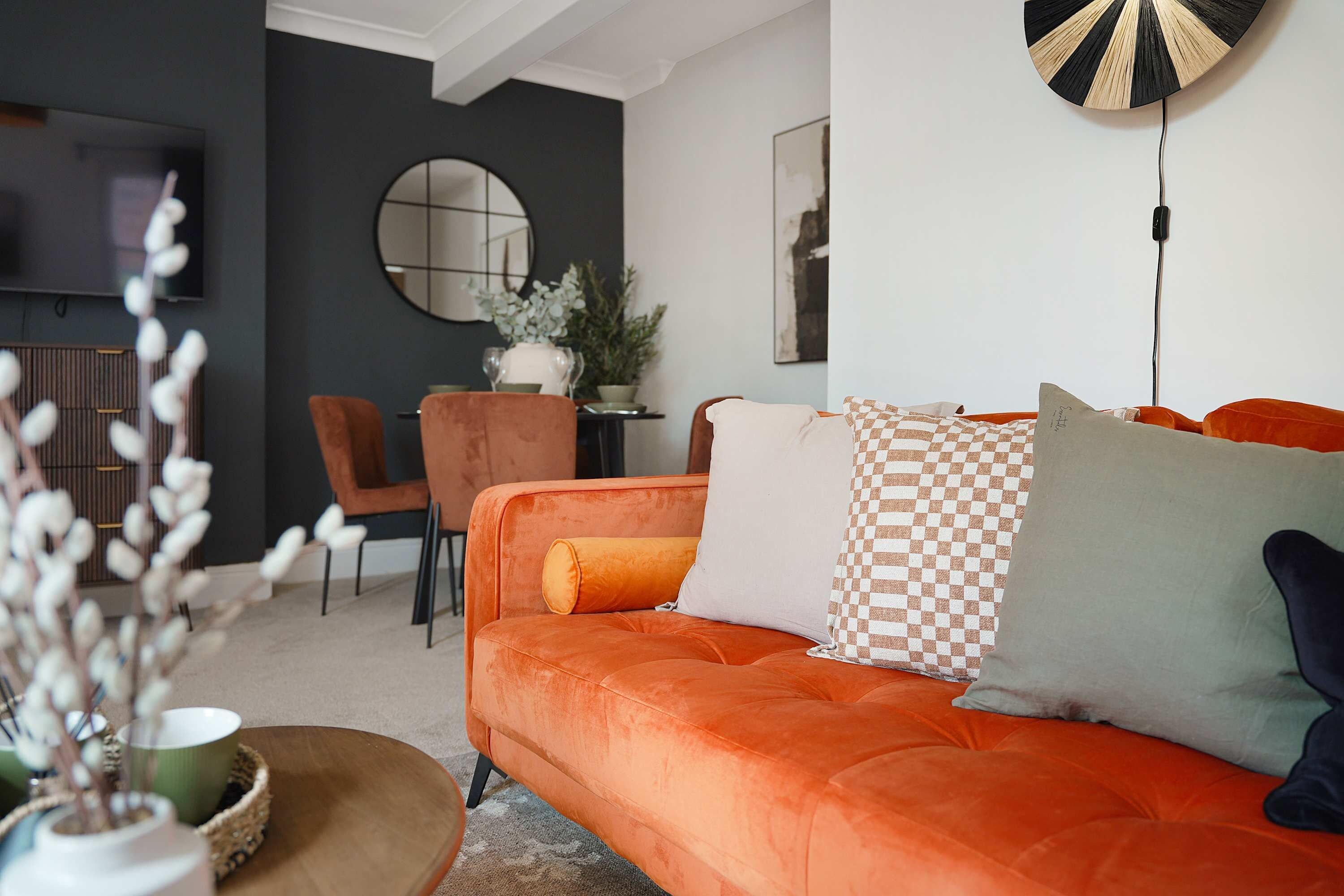 Una sala de estar moderna con un sofá, un espejo redondo y un comedor con sillas y una mesa.
