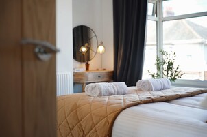 Una habitación de hotel con una cama, una mesita de noche, un espejo y una ventana con cortinas.