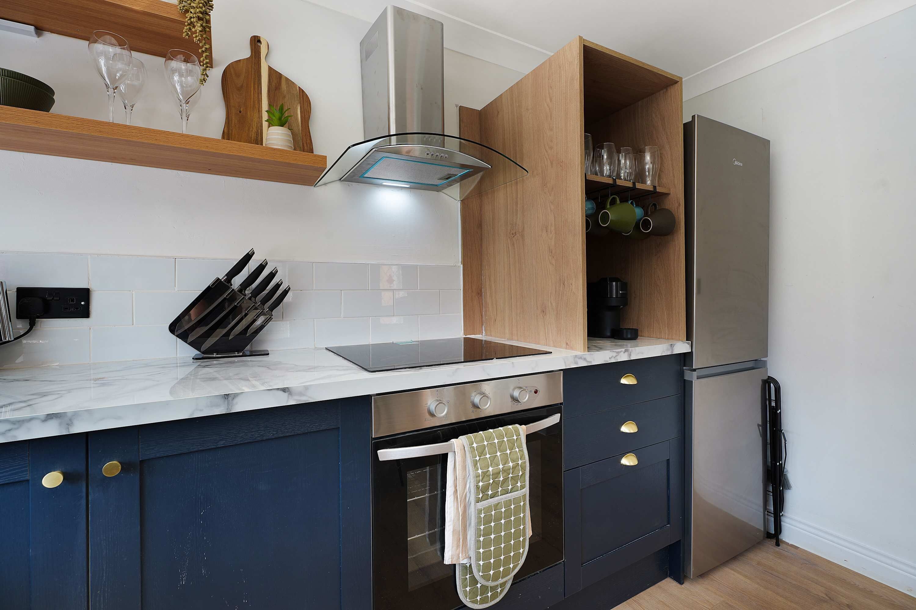 A modern kitchen with a built-in oven, a stainless steel refrigerator, and a wooden cabinet with glassware.