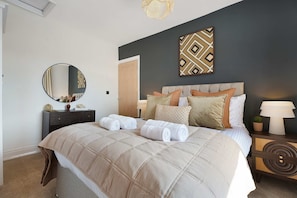 Een opgemaakt bed met een beige sprei, een nachtkastje met een lamp en een spiegel aan de muur.