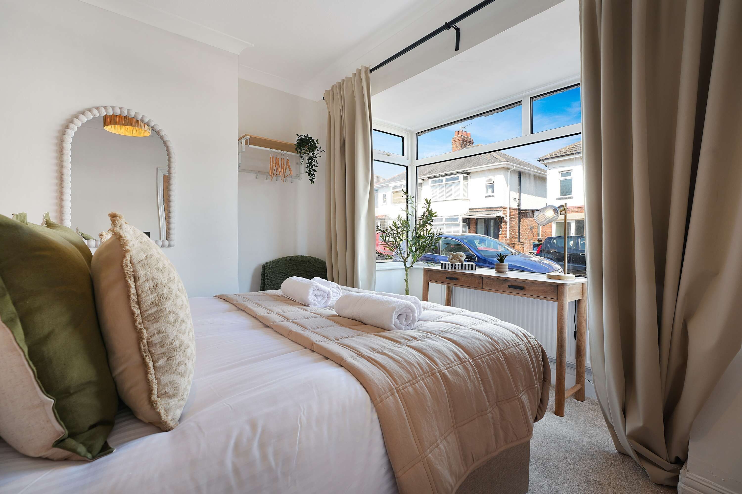 Habitación de hotel con cama, espejo, ventana con cortinas, escritorio y vista al exterior.