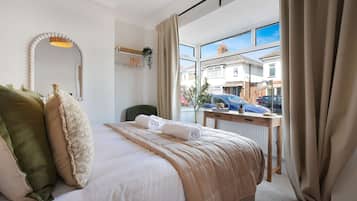 Habitación de hotel con cama, espejo, ventana con cortinas, escritorio y vista al exterior.