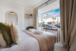 Een hotelkamer met een bed, een spiegel, een raam met gordijnen, een bureau en uitzicht op het omliggende landschap.