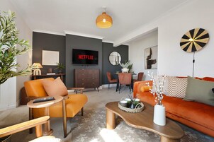Una sala de estar moderna con un sofá, sillones, una mesa de centro y un televisor que muestra el logo de Netflix.