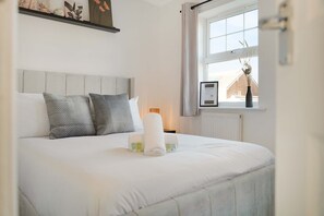 Ein ordentlich bezogenes Bett mit Kissen, ein Nachttisch mit Lampe und ein Fenster mit Blick auf ein Gebäude.