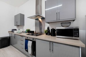 A modern kitchen with grey cabinets, a stainless steel range hood, a microwave, and a sink. - Ground-floor 2BR Newcastle Retreat Sleeps 4 (Newcastle-upon-Tyne)